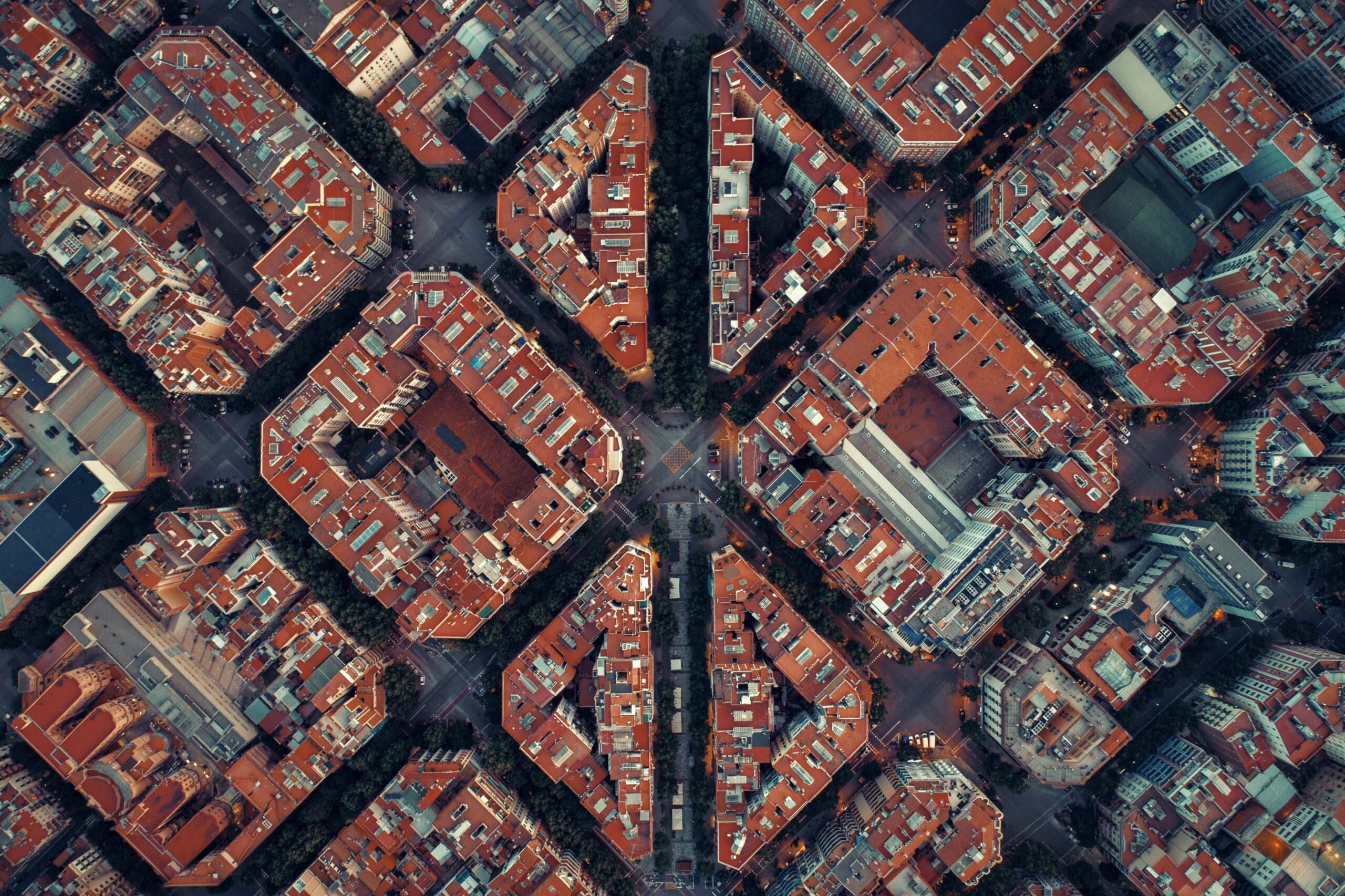 An aerial view captures a city block's grid pattern, showcasing residential buildings with red roofs and auto-draft tree-lined streets.