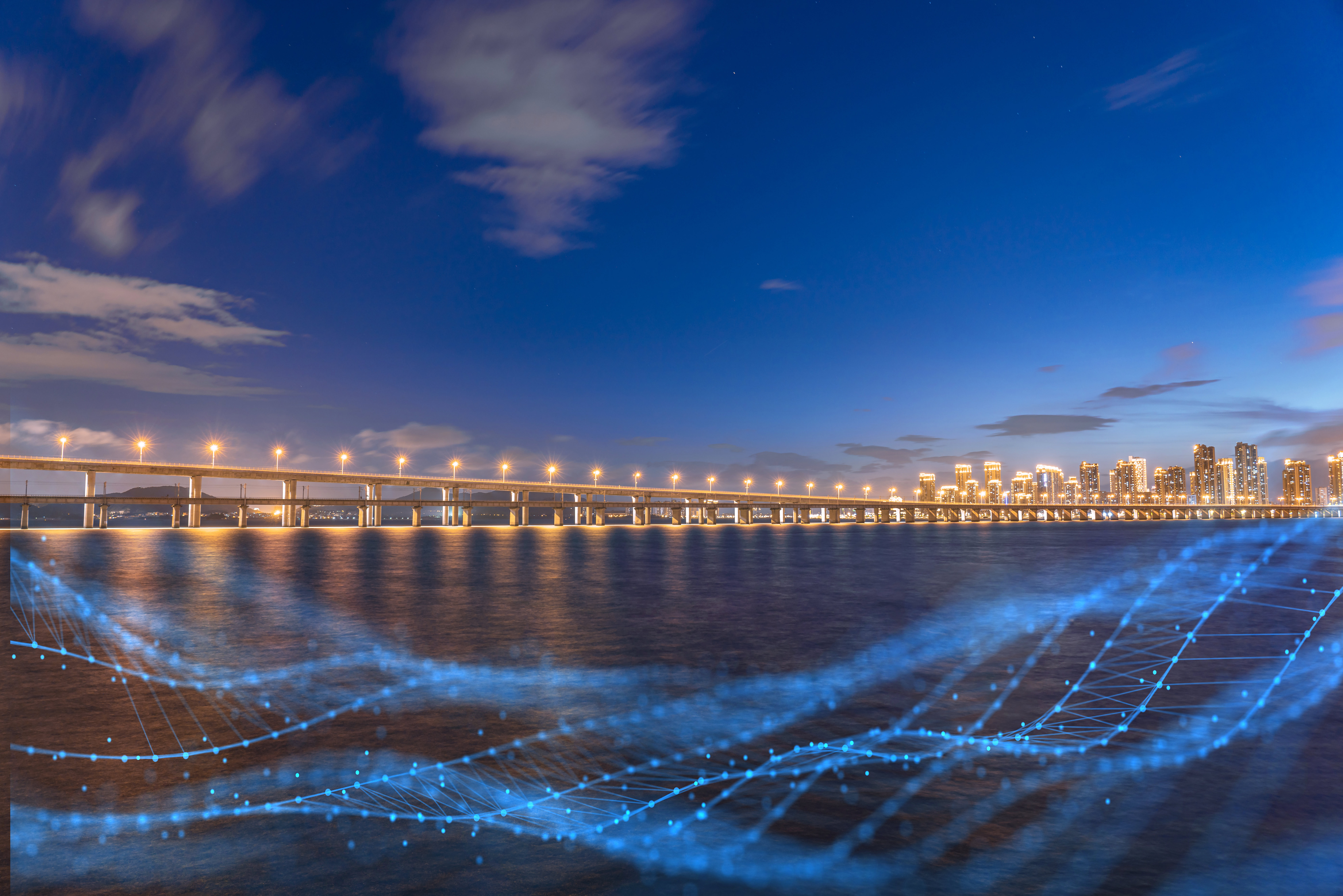 A lit bridge stretches across a body of water at dusk with a city skyline in the background. Blue digital lines and dots overlay the image, suggesting data or Auto Draft connectivity.