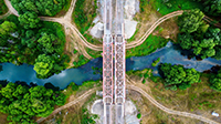 Luftaufnahme einer roten Stahlbrücke über einen Fluss mit Wegen, die problemlos zu den umliegenden üppigen grünen Bäumen führen und die Eleganz der Natur ebenso zur Geltung bringen wie professionelle Dienstleistungen die Effizienz.