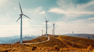 Windräder in einer hügeligen Landschaft unter teilweise bewölktem Himmel.