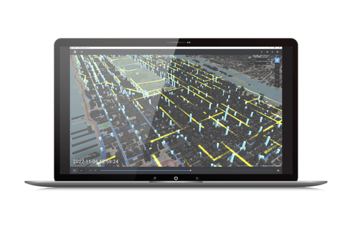 Ekran laptopa pokazujący mapę 3D z podświetlonymi budynkami i liniami siatki. W lewym dolnym rogu wyświetlany jest znacznik czasu: "2022-11-06 21:59:24.