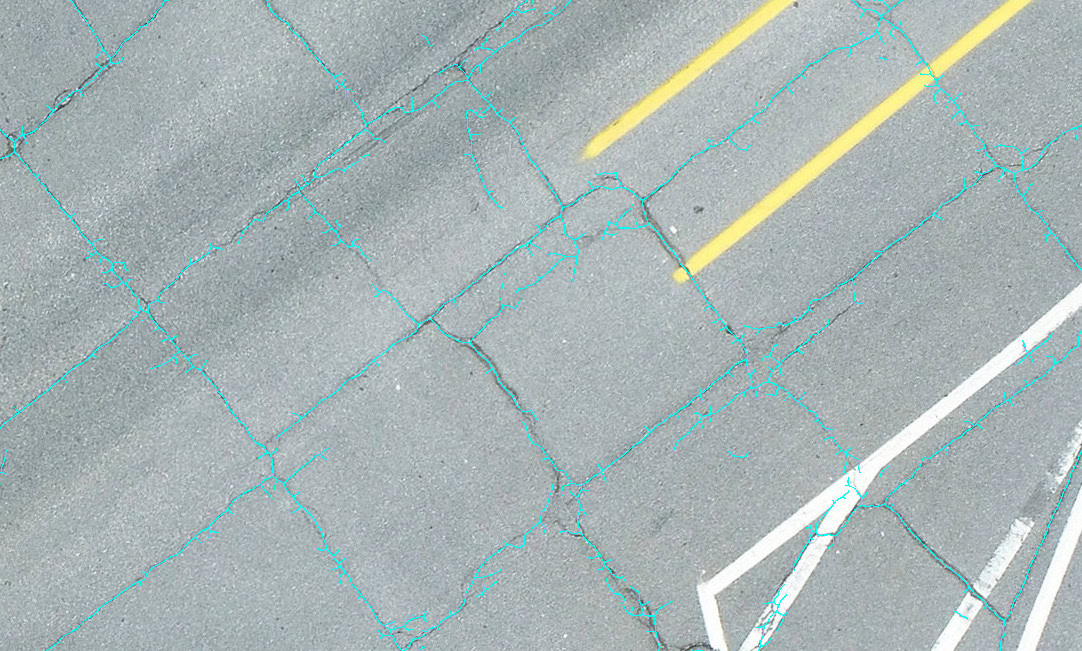 Aerial view of a cracked asphalt road with two yellow lines and a white arrow marking on the right.