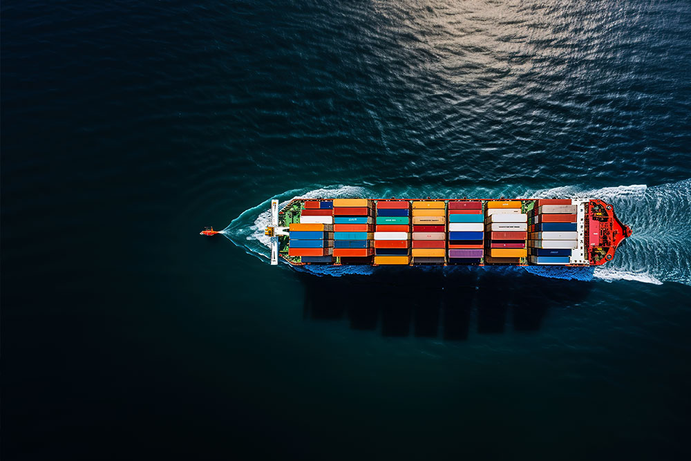 Aerial view of a large cargo ship carrying multicolored shipping containers in the ocean.