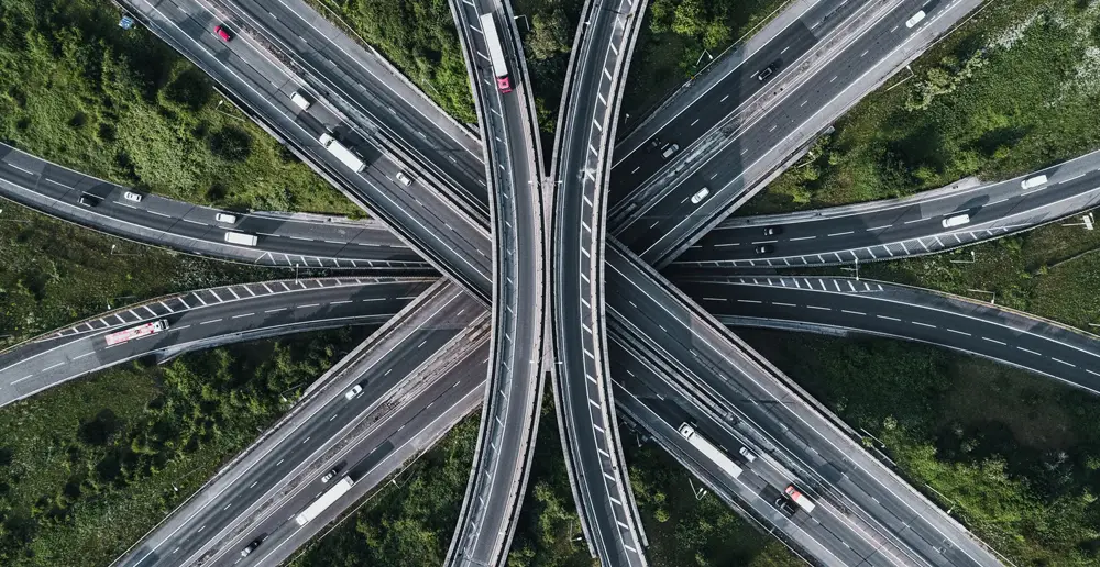 Aerial view of a highway interchange with multiple overpasses and roads weaving through lush green vegetation, resembling a network of connections akin to data services. Cars and trucks navigate in various directions, reflecting the dynamic flow of information.