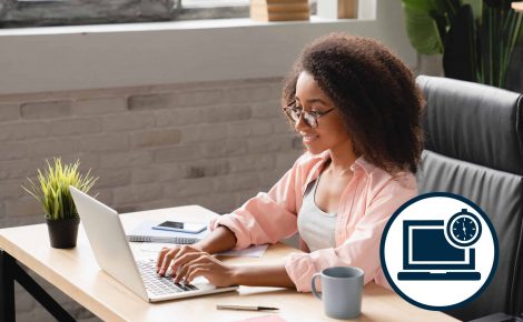 Une personne aux cheveux bouclés et à lunettes est assise à un bureau et tape sur un ordinateur portable, impatiente d'apprendre quelque chose de nouveau. Le bureau est également décoré d'une plante, d'un bloc-notes, d'un smartphone et d'une tasse à café. Une horloge et une icône d'ordinateur se trouvent dans le coin de l'image.