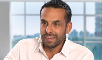 A man with short dark hair and a trimmed beard, wearing a white shirt, sits indoors by large windows overlooking a cityscape in this Geomatex Partner Spotlight.