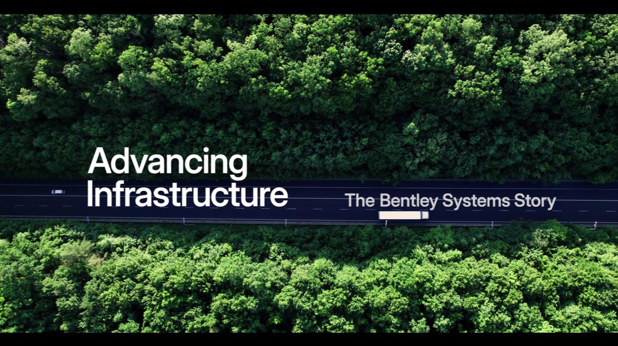 鬱蒼とした森の中を横切る道路の空中写真と白いテキストオーバーレイ: 「Advancing Infrastructure – The Bentley Systems Story.