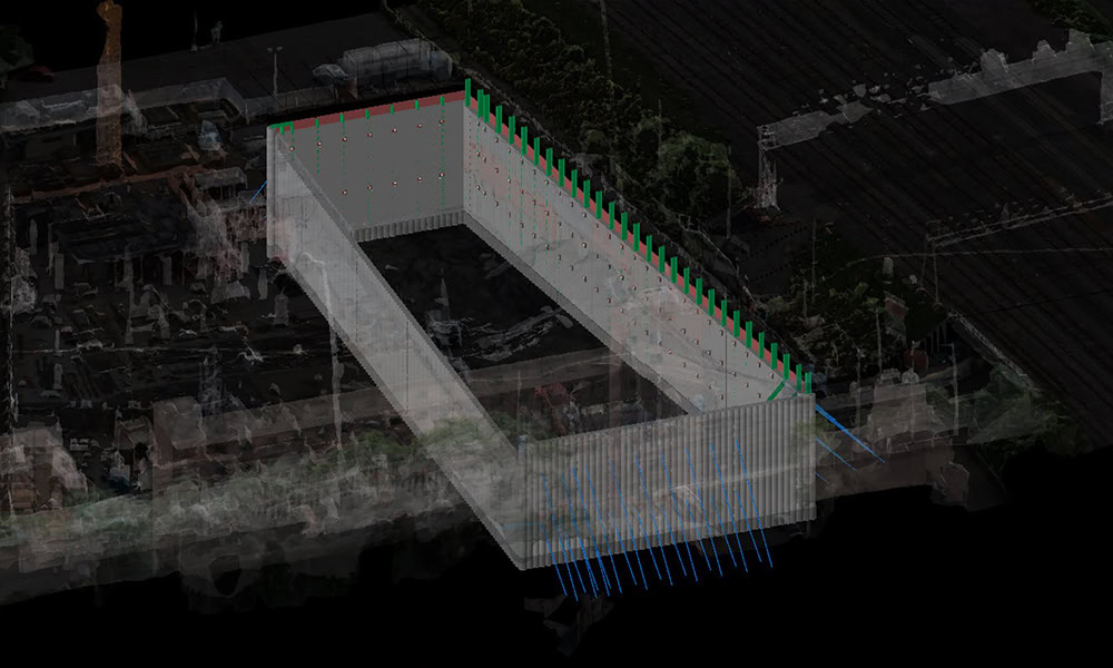 3D model of an underground construction site with rectangular walls, seen from above, surrounded by blurred structures and railway lines.