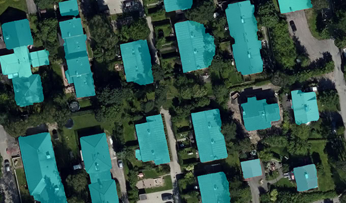 Aerial view of a residential area with houses featuring turquoise roofs, surrounded by greenery and roads.