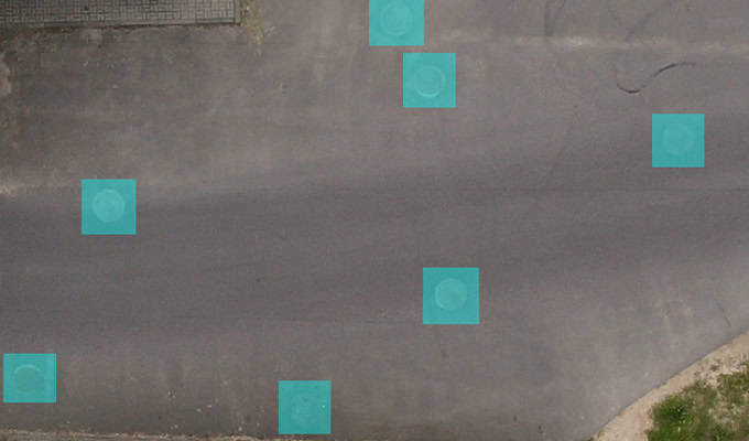 Aerial view of a road with multiple teal-colored square markers indicating specific points on the surface.