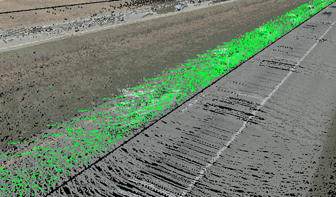 Aerial view showing a straight road with adjacent land, featuring a segment highlighted in green, possibly indicating elevation or another measurement.