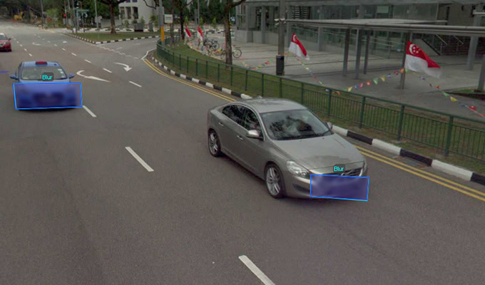 Two cars with blurred license plates drive on a road lined with Singapore flags and nearby buildings.