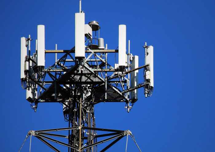 Una torre celular de telecomunicaciones diseñada por Johnson Broderick Engineering, equipada con múltiples antenas y parabólicas, se alza contra un cielo azul claro.