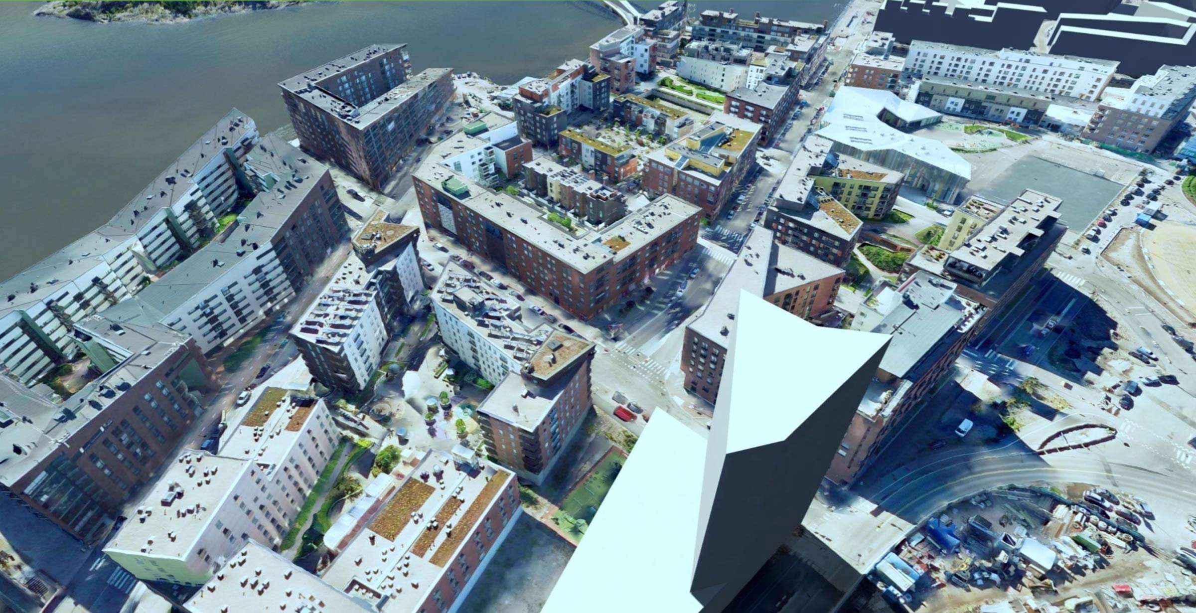 Aerial view of the City of Helsinki showcasing a mix of residential and commercial buildings along a river, with roads and green rooftops visible. The scene highlights the power of digital twin technology in urban planning and digitalization efforts.