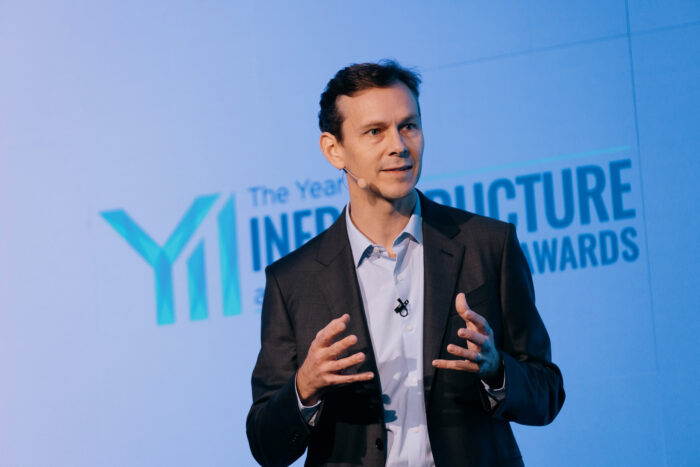 Nicholas Cumins, the CEO of Bentley Systems, speaks on stage in a suit, gesturing with both hands.