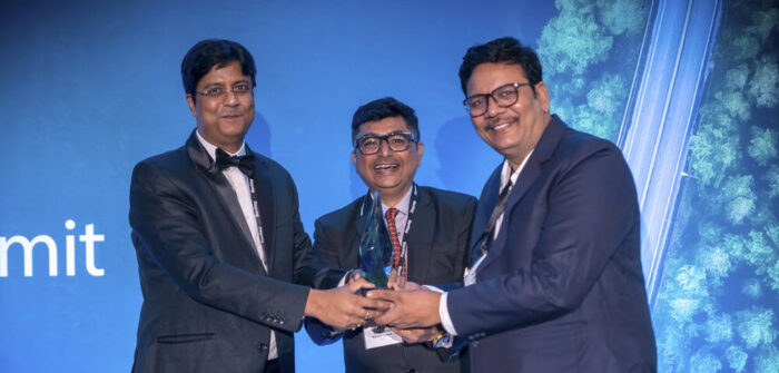 Three men in suits smiling, proudly showcasing an award, stand against a blue backdrop with the word "Summit" partially visible—it's a true Partner Spotlight moment for Mahavir Traders.