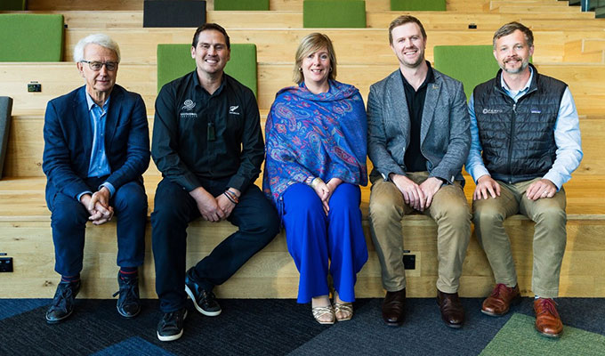 Five people from the International Geothermal Association sit on bleachers, dressed in business-casual attire, and smile at the camera, embodying their commitment to a sustainable future powered by geothermal energy.