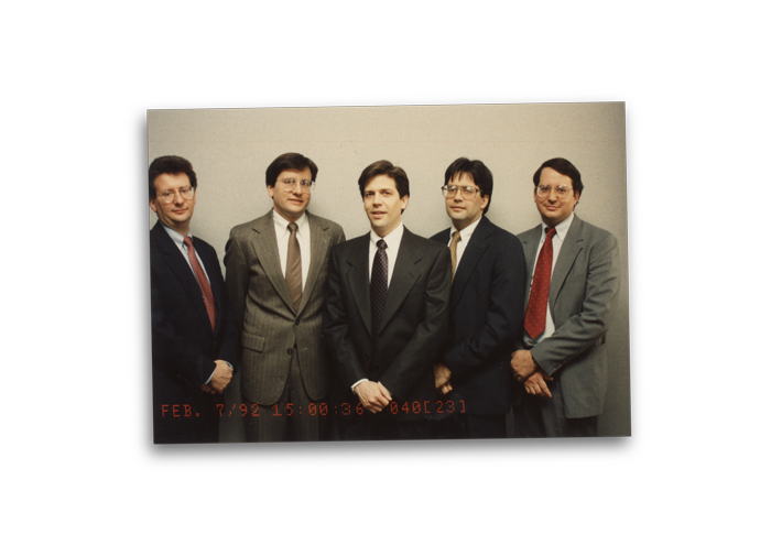 Five men in suits standing side by side, facing the camera. The date "Feb. 7, '92" and a timestamp are visible at the bottom of the image.