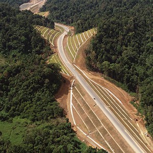 Aerial view of Lebuhraya Borneo Utara, showcasing a curved road running through a hilly forested area, with cleared sections of land on either side.