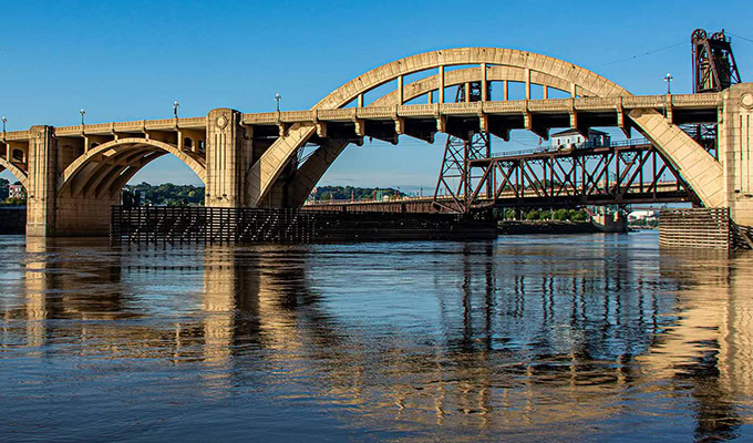 A train crosses an arched bridge over a calm river, surrounded by clear blue skies, symbolizing sustainability in motion as it embraces eco-friendly action.