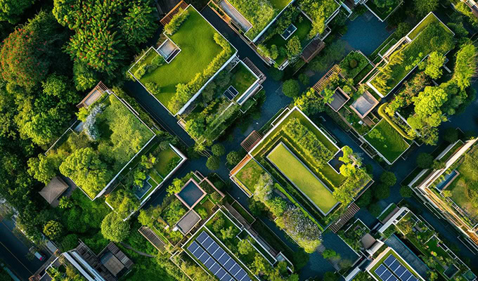 Aerial view of buildings with lush green rooftops and solar panels surrounded by trees, showcasing sustainability and representing an eco-friendly urban environment in action.