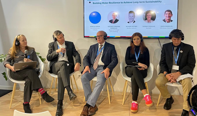 Five panelists seated under a display screen discussing water resilience at an event.