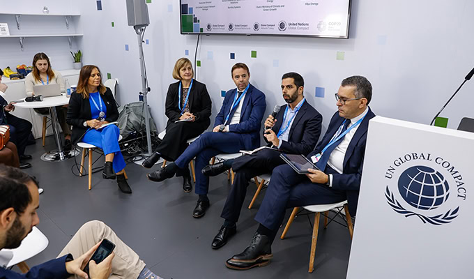 A panel of five people sits in a row speaking at a UN Global Compact event. Audience members are visible in the foreground.