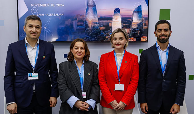 Four people in business attire stand in front of a screen displaying "November 16, 2024, Baku - Azerbaijan.