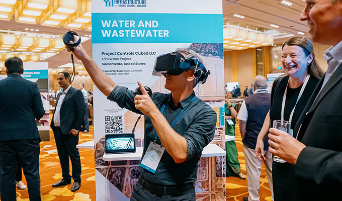 A person uses a VR headset in front of a "Water and Wastewater" conference booth, surrounded by other people.