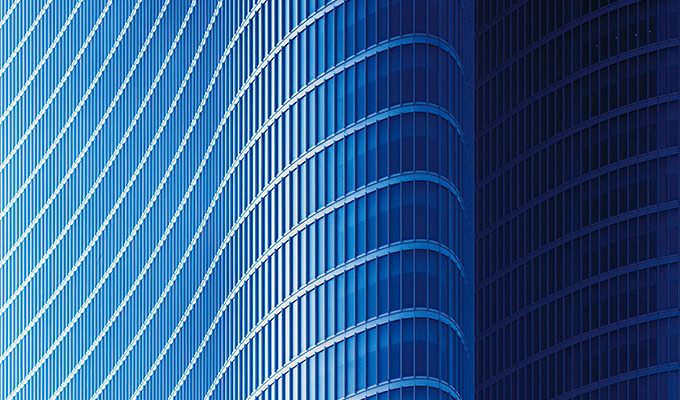 The curved blue glass façade of this modern building, inspired by action-driven sustainability, features vertical lines that create a wave-like pattern.