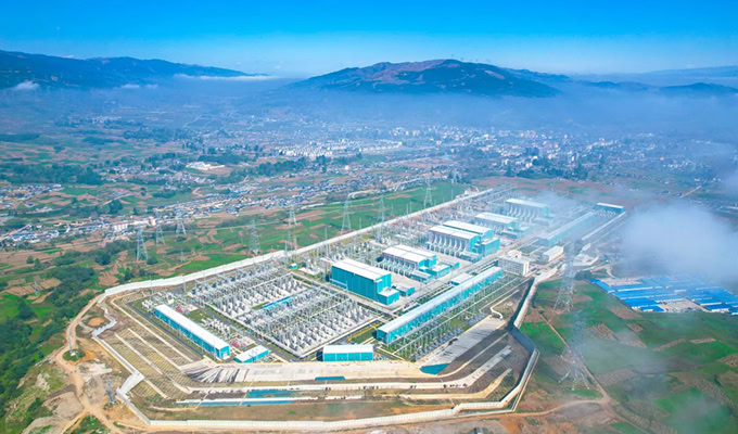 Aerial view of a large industrial complex with multiple buildings, surrounded by green fields and mountains in the distance, showcasing a commitment to sustainability through eco-friendly practices.