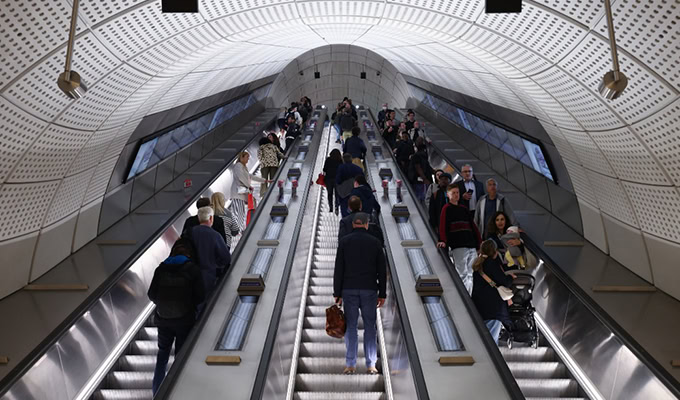 People are using escalators in a well-lit subway station with a curved ceiling, taking deliberate actions towards sustainability by choosing efficient public transport.