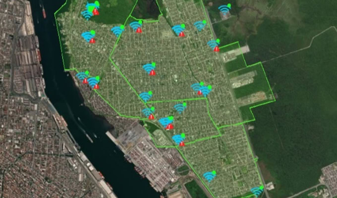 Mapa satelitarna przedstawiająca obszar miasta z nałożonymi ikonami wskazującymi sygnały Wi-Fi i alerty w całym regionie. Rzeka i strefy przemysłowe są widoczne po lewej stronie, podkreślając obszary, w których zrównoważone działania są niezbędne.