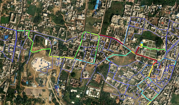 Uma visão aérea de satélite de uma área urbana com várias linhas coloridas cobrindo as ruas, sugerindo diferentes marcações de rota ou planos de infraestrutura.