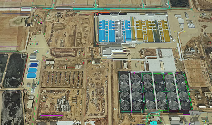 Vue aérienne d'une grande installation industrielle comprenant plusieurs bâtiments, des réservoirs de stockage, des zones de construction et son infrastructure environnante.