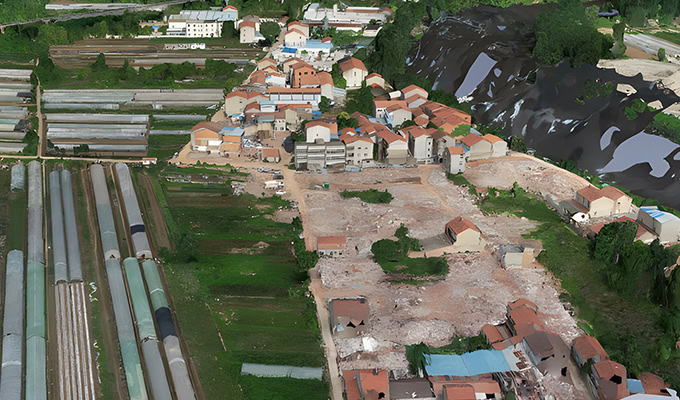 Vista aérea de uma pequena cidade com fileiras de estufas, edifícios residenciais e uma grande área limpa com entulho. A vegetação circundante e as colinas são visíveis.