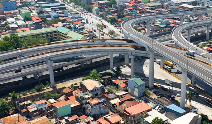 Vista aérea de uma rodovia elevada com vários viadutos em uma área urbana com prédios densamente lotados e estradas abaixo.