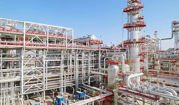 A large industrial complex with extensive piping, metal structures, and multiple tanks and towers under a clear blue sky.