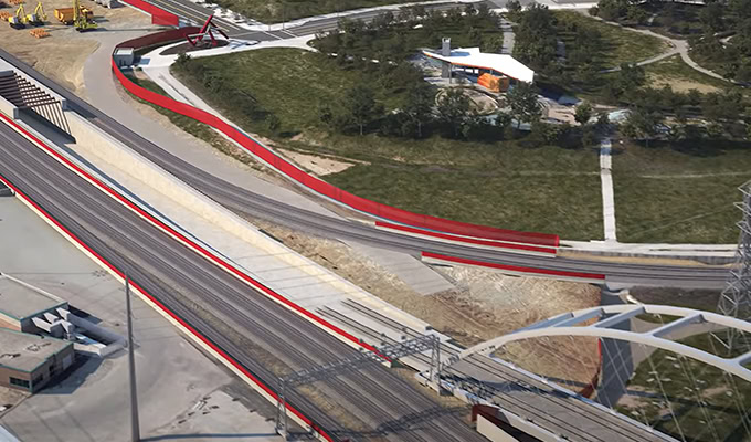 Aerial view of a railway construction site featuring multiple tracks, red safety barriers, nearby construction equipment, and adjacent green spaces.