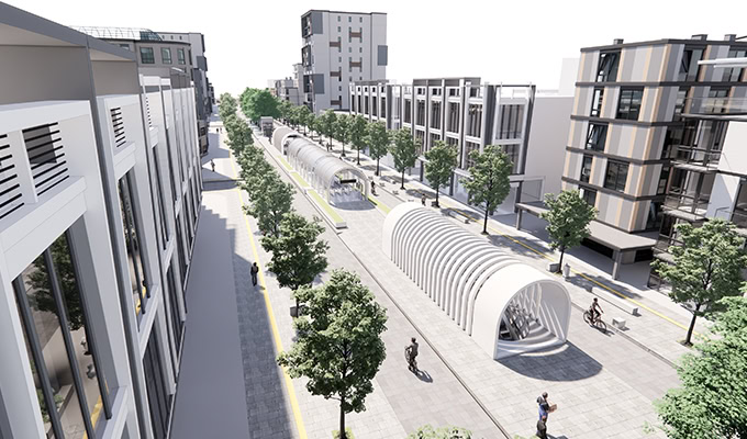 Una calle urbana moderna con aceras arboladas, edificios de mediana altura y una pasarela peatonal con estructuras aireadas en forma de túnel.