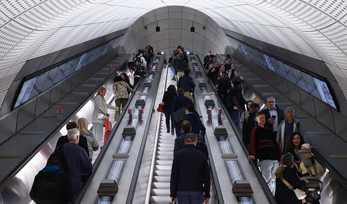 Menschen, die auf langen Rolltreppen in einer gut beleuchteten, modernen U-Bahn-Station auf und ab fahren.