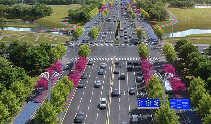 Un'ampia strada cittadina a più corsie con traffico intenso. La strada è fiancheggiata da alberi con fiori rosa e fogliame verde lussureggiante. Piste ciclabili e passerelle pedonali corrono parallele alla strada.