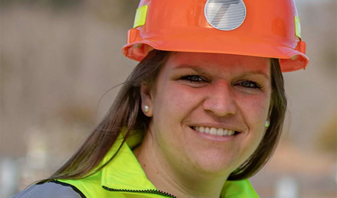 A person wearing an orange hard hat and a high-visibility jacket smiling at the camera.