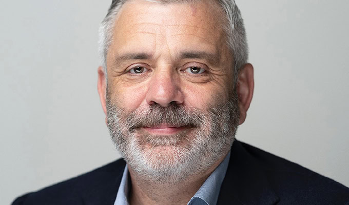 Middle-aged man with short gray hair, a gray beard, and wearing a dark suit jacket and blue shirt. He is looking into the camera with a neutral expression.